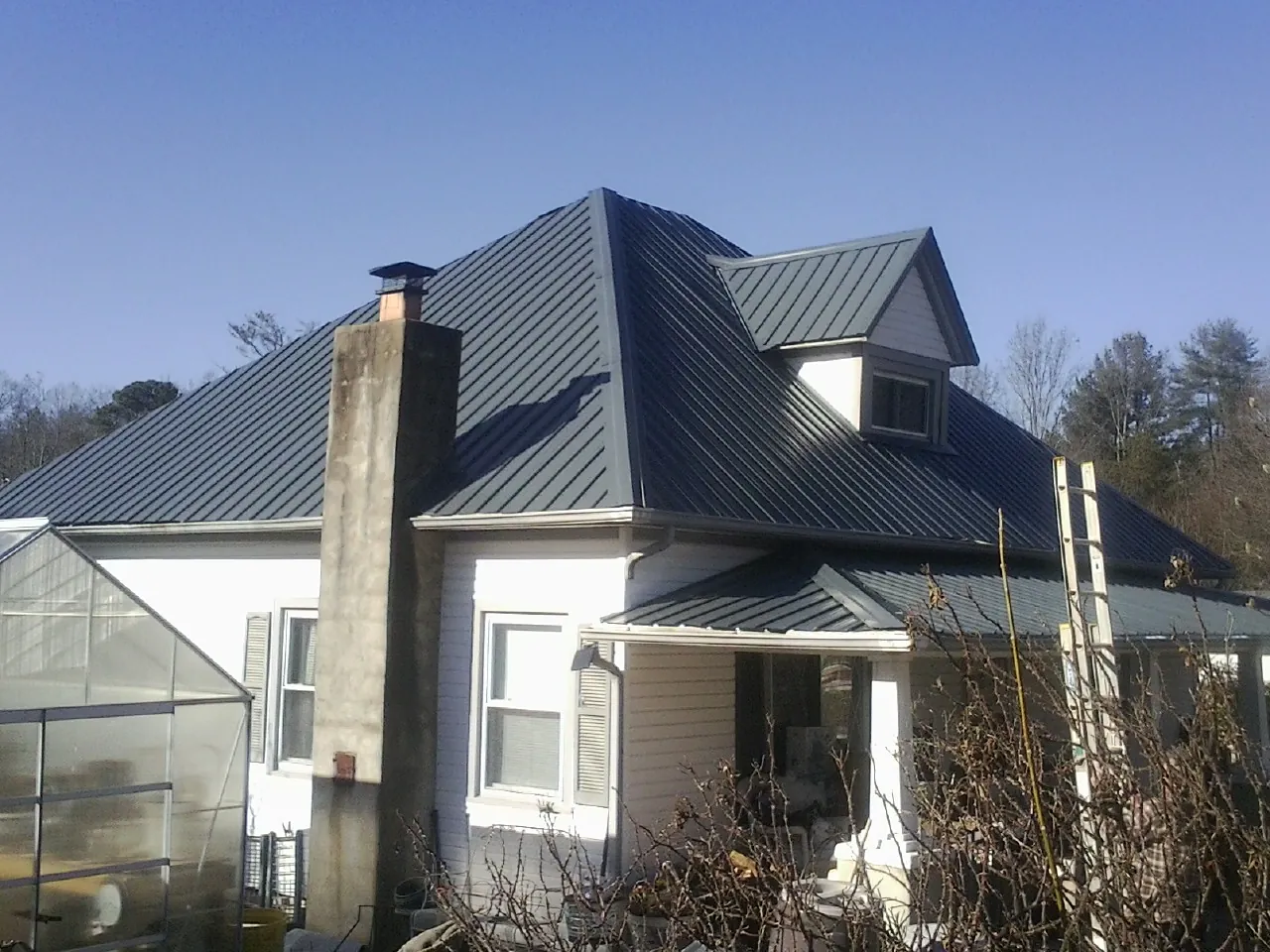Dark blue standing seam metal roof on a white farmhouse with dormer — Slate & Tile Roof Repair by Roofing Brothers in Langeloth