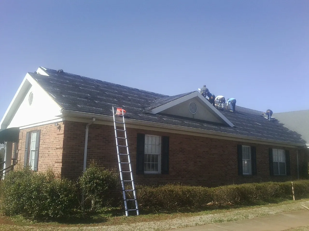 Crew tearing shingles off a brick ranch roof with a ladder set — Emergency Roof Repair work by our crew in Langeloth