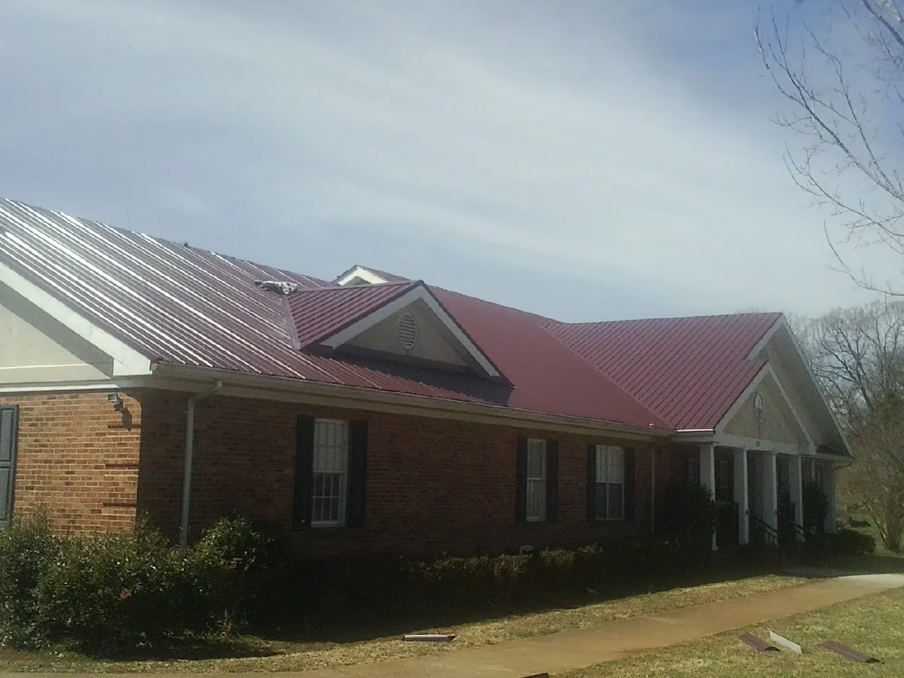 Red metal roof with gabled entries on a long brick building, from a Hail Damage Roof Repair job in Langeloth