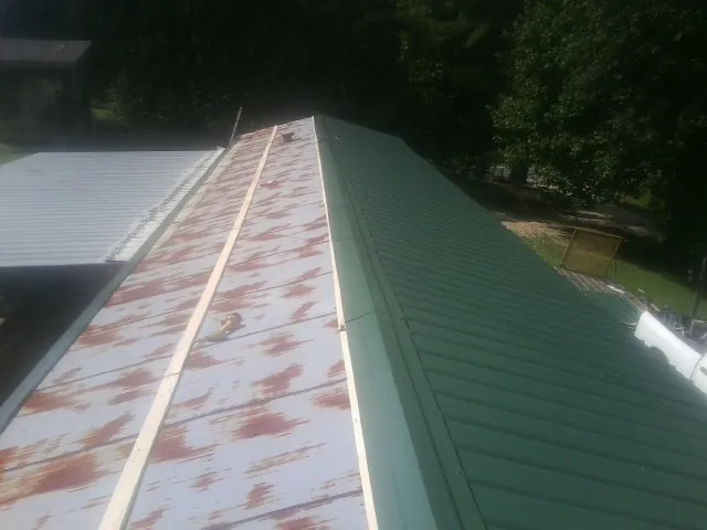 Old rusted panels beside newly installed green metal roofing — Wind Damage Roof Repair by Roofing Brothers in Langeloth