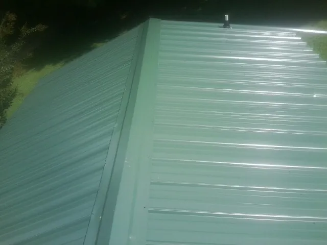 New green metal panels meeting at the ridge of a roof — Flat Roof Repair work by our crew in Langeloth