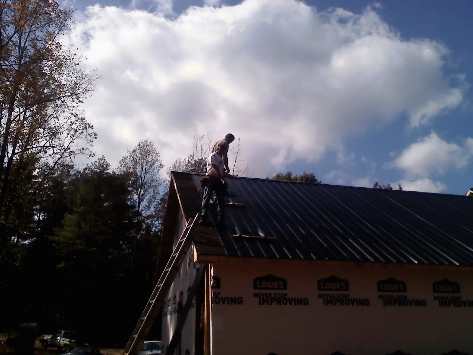 Roofer fastening dark metal panels high against a cloudy sky, from a Roof Inspection job in Langeloth
