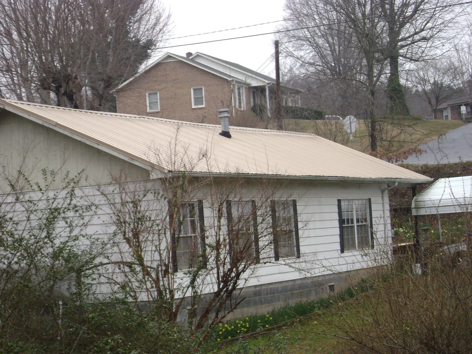 Tan metal roof on a white sided house set into a hillside — Commercial Roofing by Roofing Brothers in Langeloth