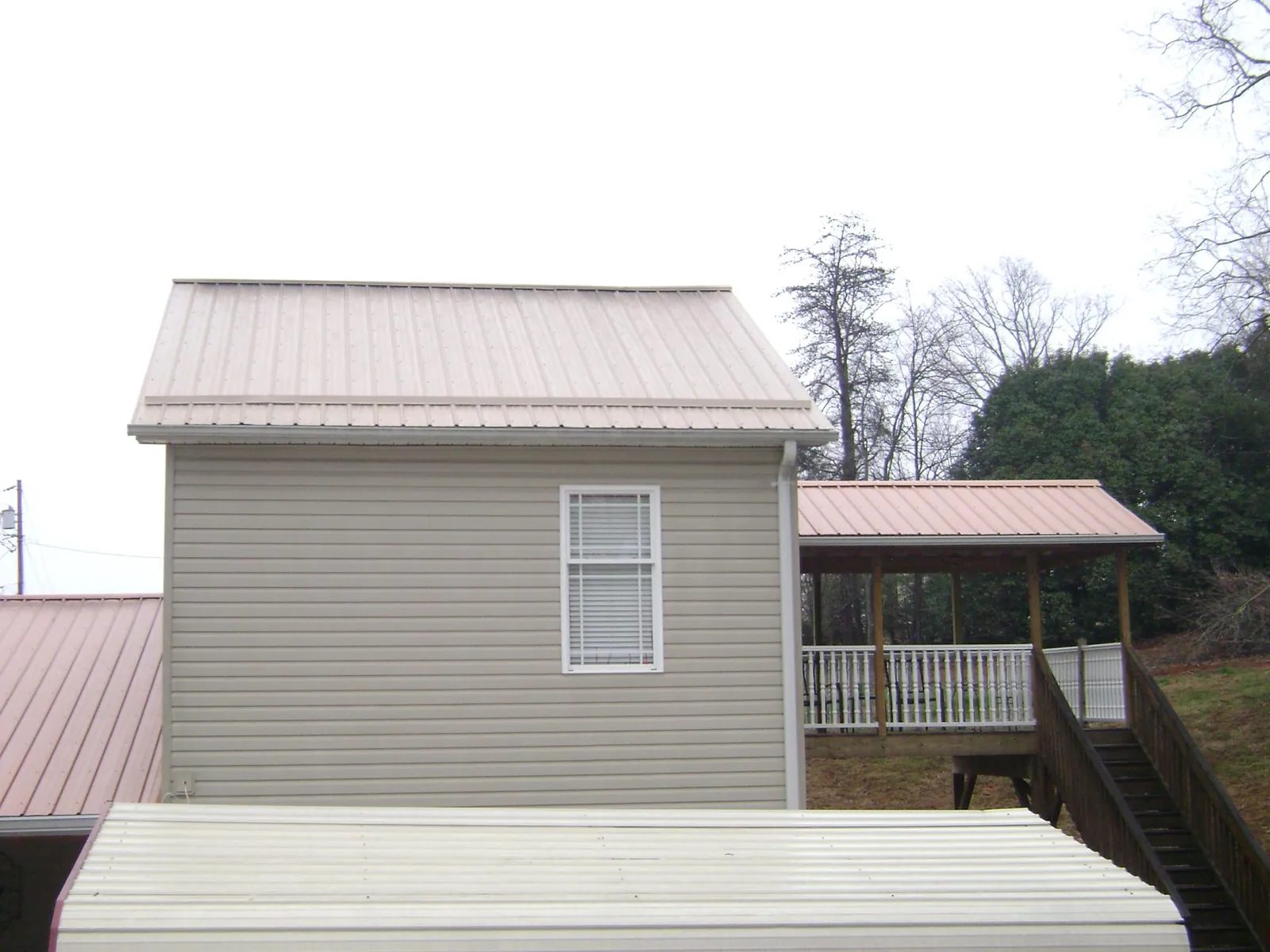 Tan metal roofs on a two story addition and attached porch, from a Roof Replacement job in Langeloth